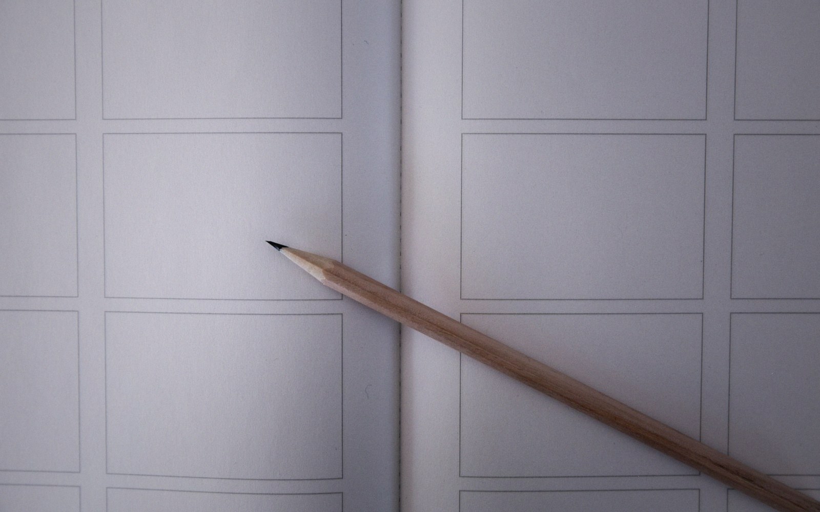 A sharpened pencil resting across a blank storyboard notebook with empty grid panels
