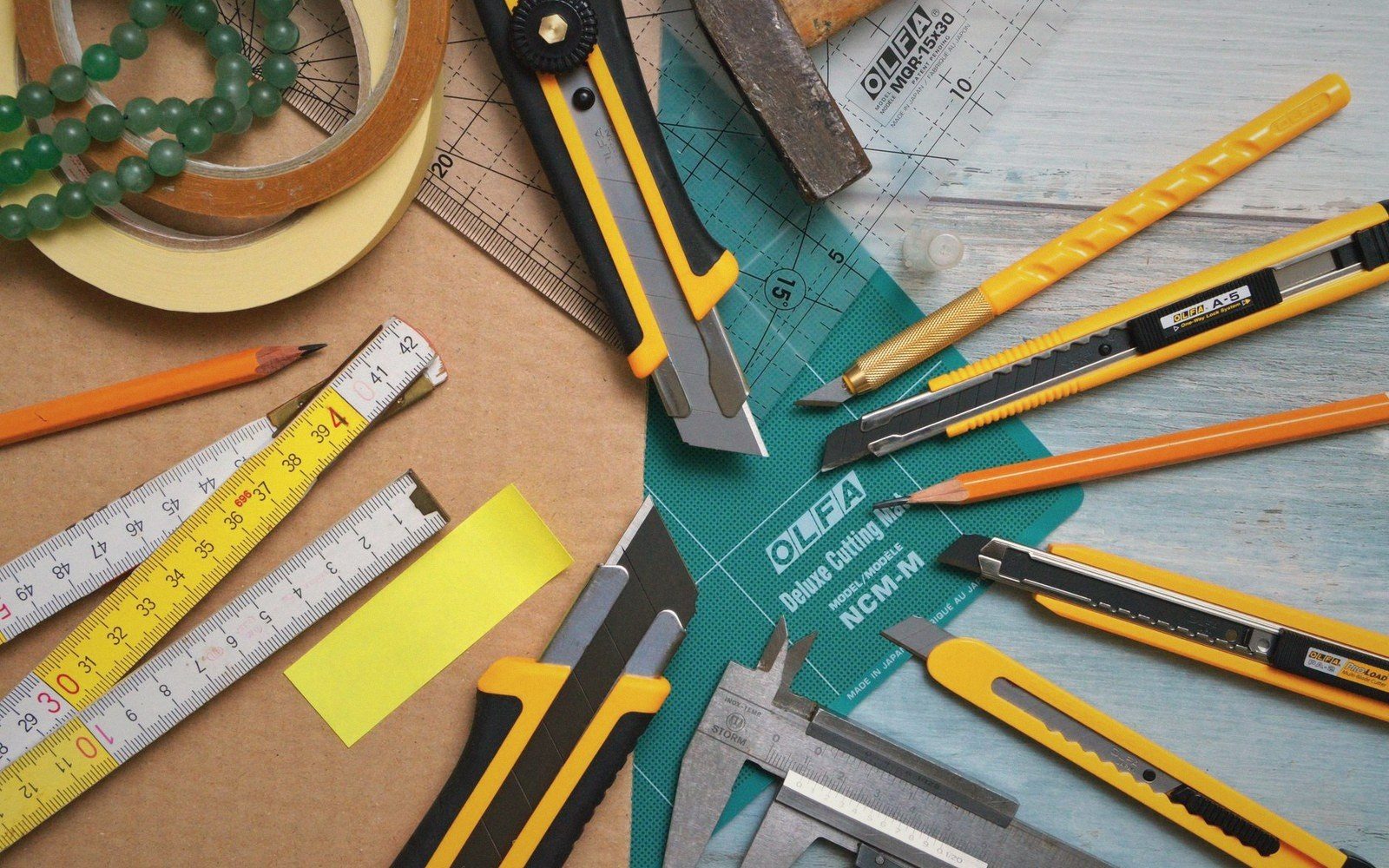 Utility knives, folding rulers, calipers and pencils arranged around a cutting mat