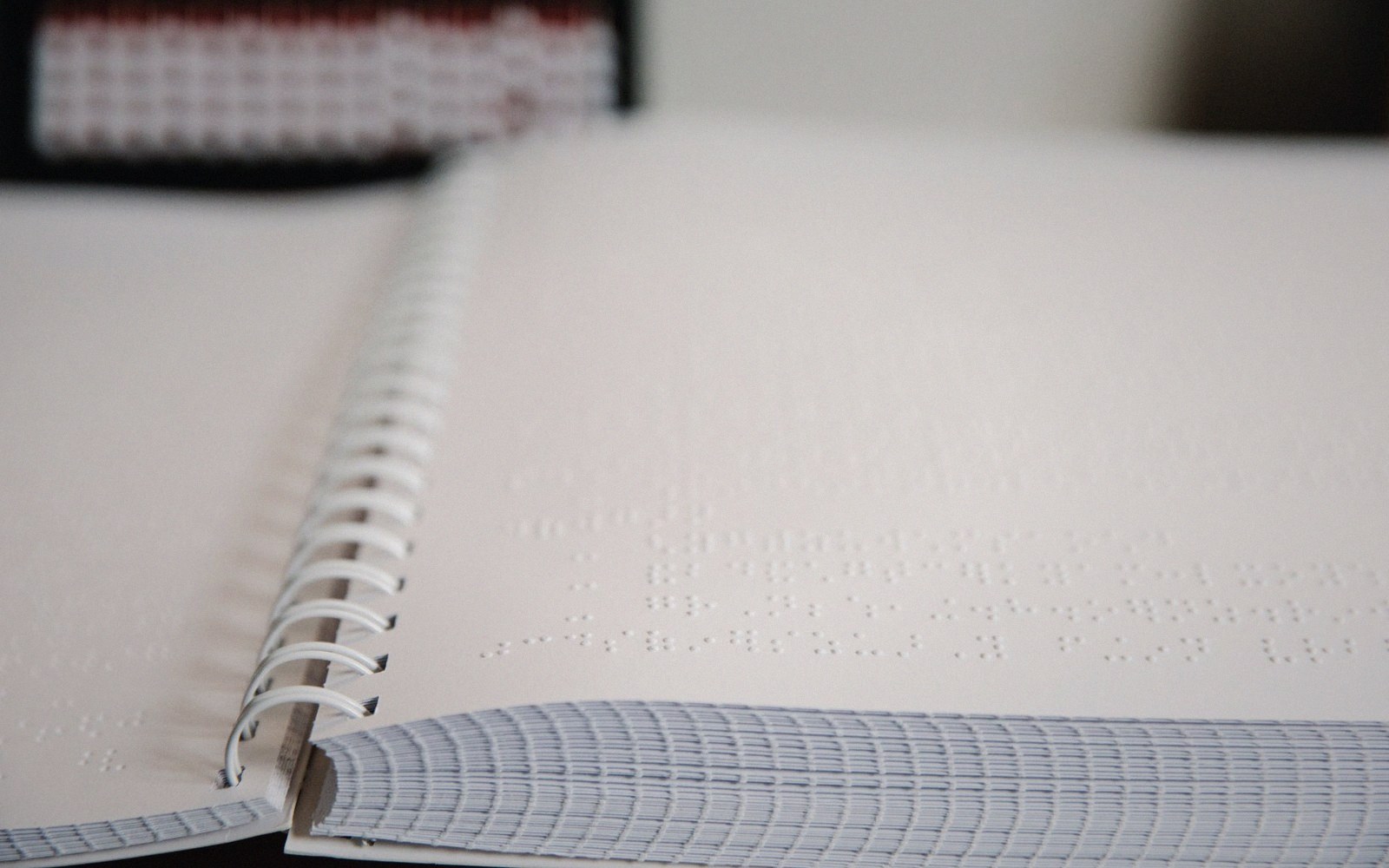 Open spiral-bound notebook with embossed braille text on a blank page