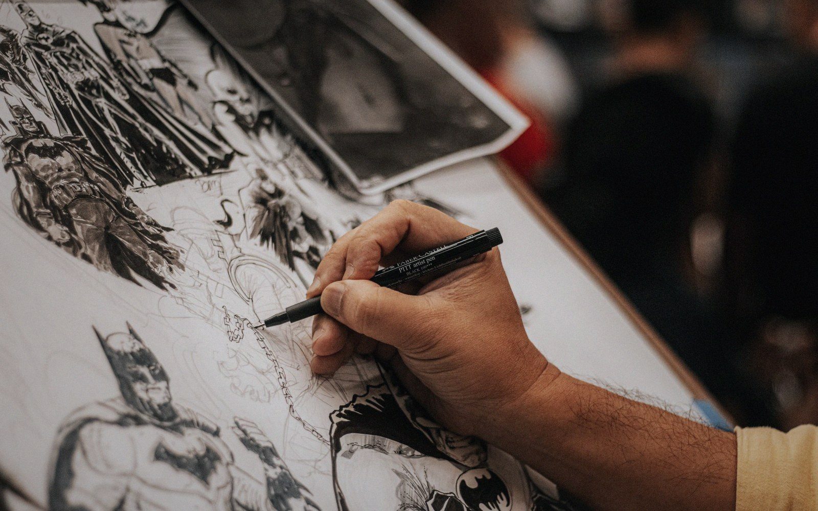 An artist inks a detailed Batman illustration with a fine-tipped pen